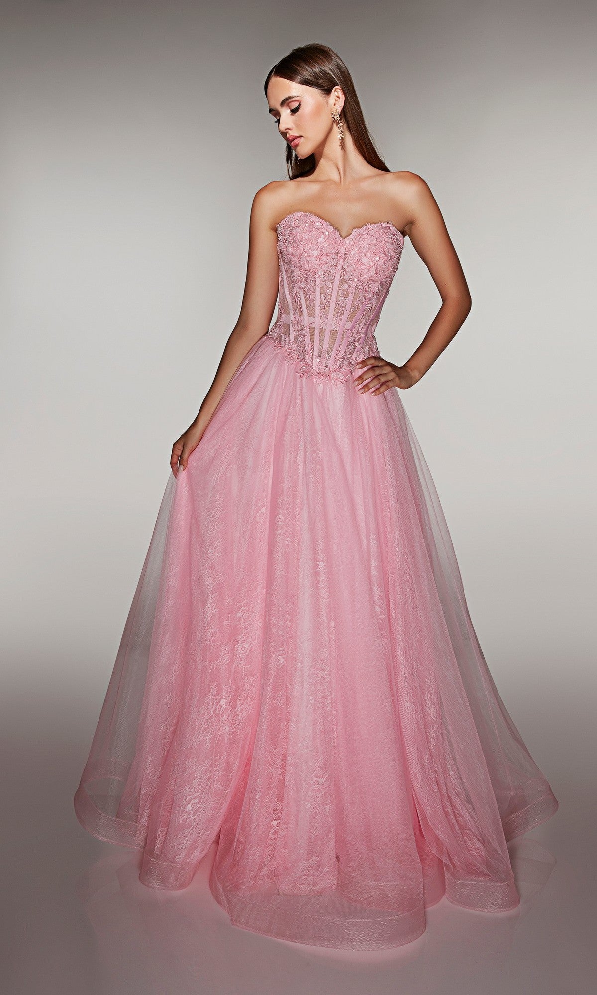 A woman models the Alyce 61984 long prom dress, featuring a strapless fitted lace corset bodice and a voluminous tulle ball gown skirt, standing against a plain background.